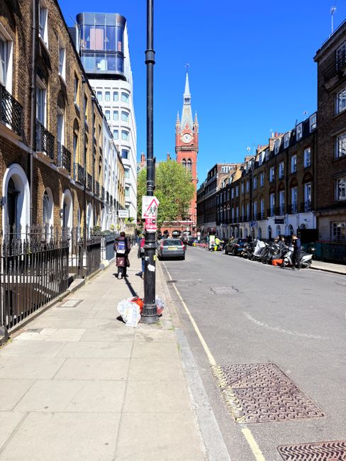 A street scene featuring a variety of historic buildings with architectural details including large windows, ornate cornices, and varied facades made of brick, stone, and plaster. The primary building